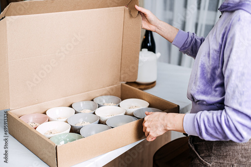 Packing Homemade Oatmeal Bowls in Cardboard Box. Person carefully packing multiple bowls of homemade oatmeal into a large cardboard box for delivery or convenient distribution.