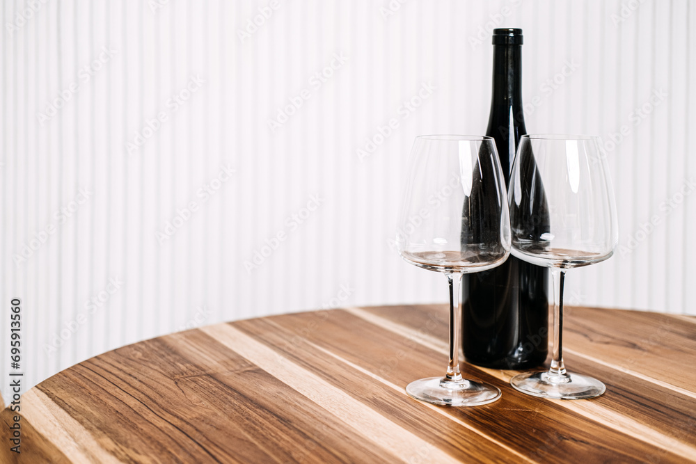 Minimalist Wine Bottle and Glasses on Wooden Table. A simple yet elegant setup of a wine bottle and two glasses on a polished wooden table against a striped background.