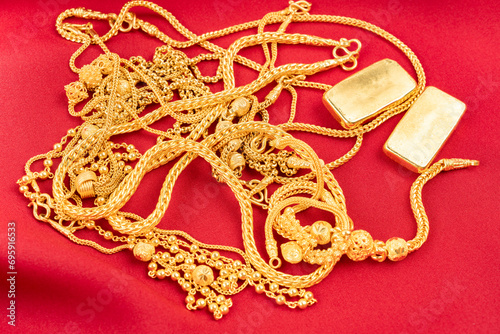 Many gold necklaces and gold bars on red velvet cloth.