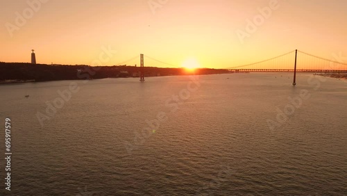 Aerial view of Tagus river at sunset. The 25 April Bridge and the statue of Christ in the background. Lisbon, Portugal. High quality 4k footage photo