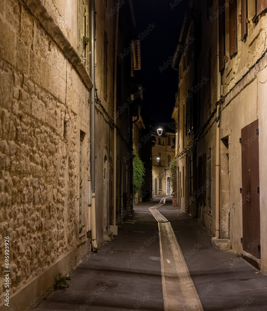 Narrow street in the old part of Arles, France, called La Roquette. Night picture, street lamps, chiaroscuro atmosphere.