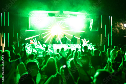 Crowd of people attending a musical performance with hands up in the air. Bright neon green light rays coming from the stage