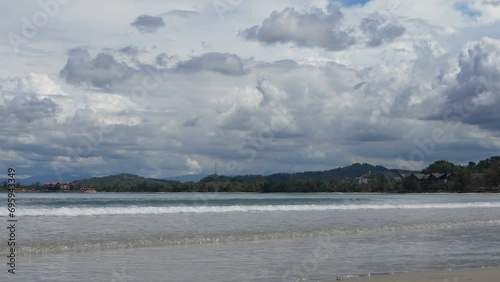A summer day in the tropics. The waves of the turquoise ocean roll towards the shore, foaming. Clear water spreads over the wet sand, bubbling.  The cottages of the hotel among the green vegetation.
