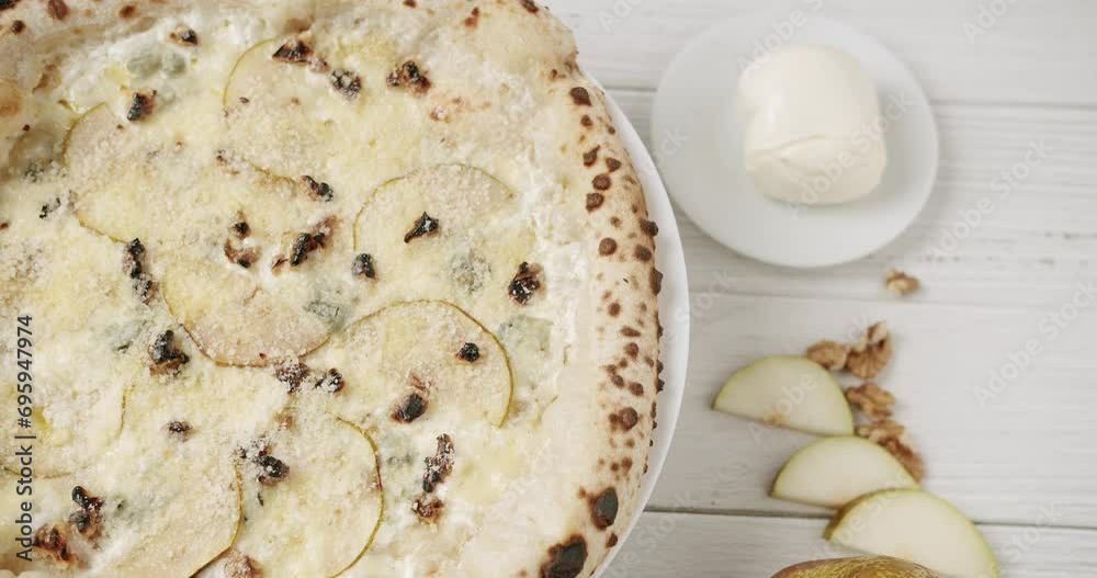 Top view on fresh pizza quattro formaggi with mozzarella, parmesan and gorgonzola served on rotating stand. Italian tasty pizza four cheese with pear and walnut on plate near ingredients on table