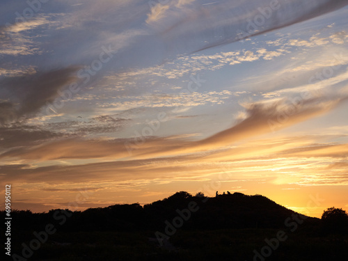 Sunset with silhouette of some people on the dunes.