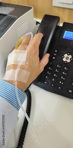 Sick doctor's left wrist with intravenous medicine injection. He still tough working despite got sick in hospital office with long sleeve blue shirt and white gown