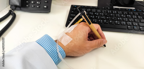 Sick doctor's left wrist with intravenous medicine injection. He still tough working despite got sick in hospital office with long sleeve blue shirt and white gown