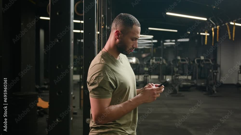 American Latino ethnic man browsing smartphone serious athlete fit sport guy personal fitness trainer instructor male in gym bodybuilder sportsman using mobile phone looking at camera happy smiling