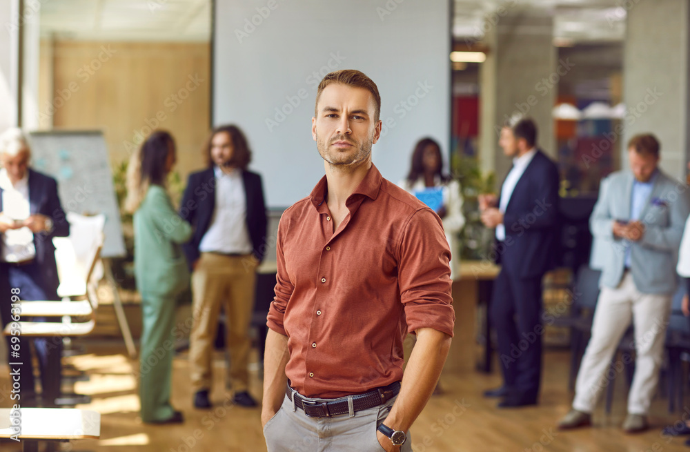 Portrait of young businessman, corporate employee or team coach at professional business training event. Serious unsmiling handsome young man in brown shirt standing in office and looking at camera