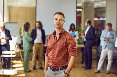 Portrait of young businessman, corporate employee or team coach at professional business training event. Serious unsmiling handsome young man in brown shirt standing in office and looking at camera photo