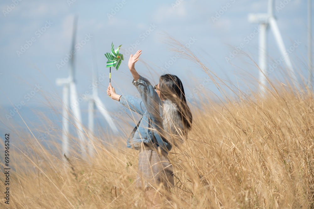 Young gorgeous brunette woman with long hair wearing a blue jacket, black sunglasses, and holding a miniature windmill