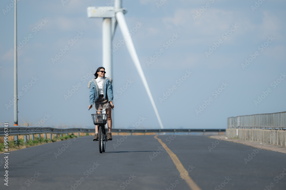 Young woman riding a bike on a road in a windmill.