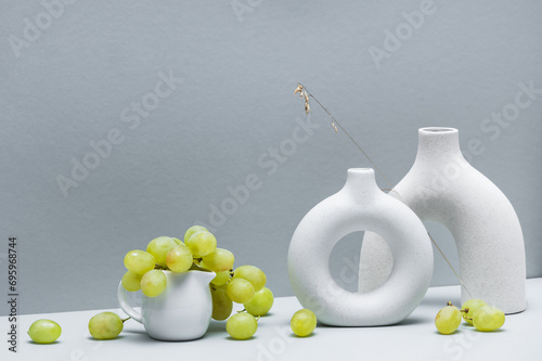 Still life with two ceramic vases and a mug of grapes on a grayish background. Space for text. photo