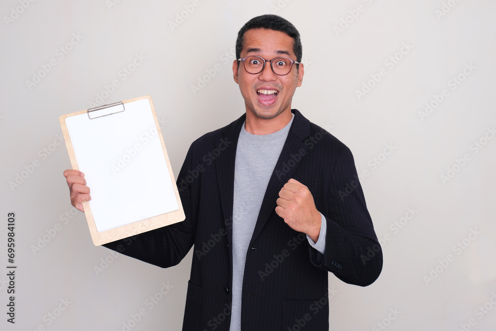 Asian businessman clenched fist showing amazed expression and holding blank paper on clipboard Asian businessman clenched fist showing amazed expression and holding blank paper on clipboard