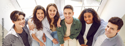 Cheerful diverse school friends having fun together. Banner with group portrait of happy multiethnic teenagers. Multiracial boys and girls sitting on window sill, looking at camera and smiling photo