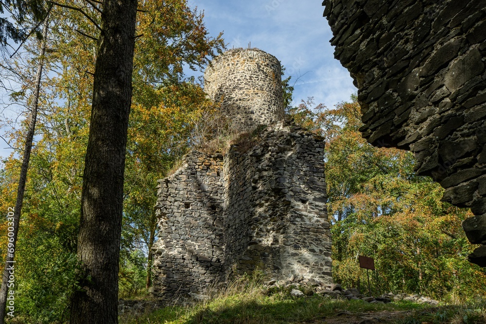 Cernosin, Czech Republic - October 13 2023: View of the ruined castle Volfstejn standing on a hill in the forest. Stone tower and the wall under reconstruction. Sunny autumn day with blue sky.