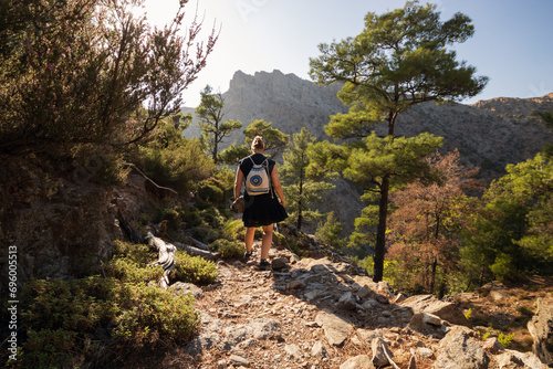 Back view of a backpacker girl hiking on a mountain trail in the lush Halari canyon on the mountainuous North Aegean Island of Ikaria.