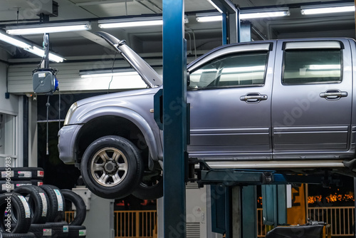 Pickup truck lifted into the air using a mechanical bridge jack in a service garage for car repair and maintenance at night time
