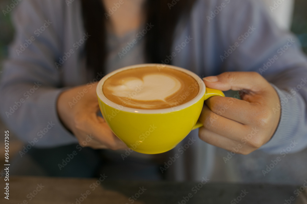 Closeup image of a cup of coffee with heart shape latte art, young woman drinking coffee in coffee shop. Soft focus. Closeup image of a cup of coffee with heart shape latte art, young woman drinking coffee in coffee shop. Soft focus.