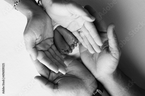 The palms of the parents, father and mother hold the legs, feet of a newborn baby. Feet, heels and toes of a newborn child close -up. Professional macro photo. Black and white. 