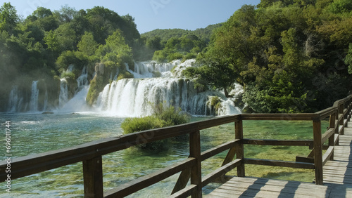 A majestic waterfall cascades down a lush forest, surrounded by towering trees and vibrant plants, as the clear water glistens under the bright sky at this tranquil state park