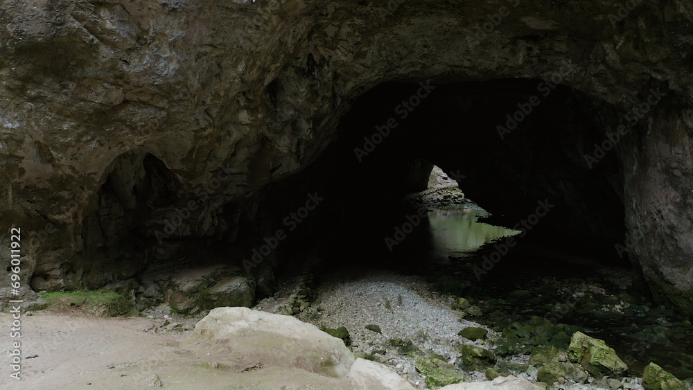 Obraz premium A hidden world of wonder and tranquility, the cave reveals the timeless beauty of nature's relentless erosion amidst the solid embrace of earth and rock, with the gentle melody of a river as its soun