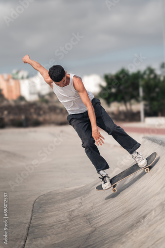 young man with white t-shirt skating in a ramp of a skate park. vertical composition