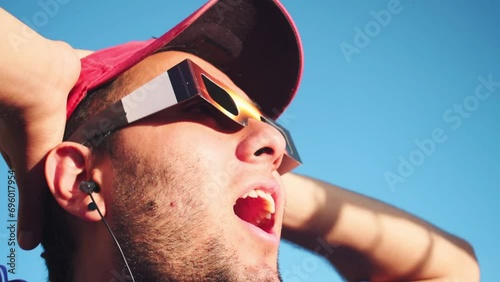 Portrait of man wearing cap and solar eclipse glasses, looking sun with blue sky at background  photo