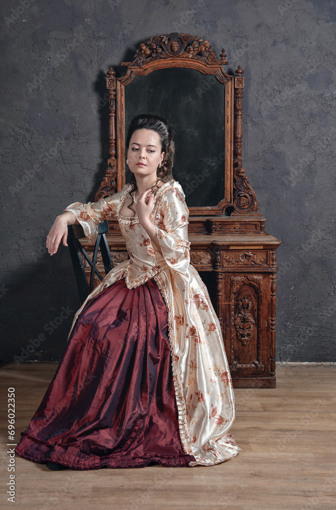 Beautiful woman in rococo style medieval dress sitting near console mirror table