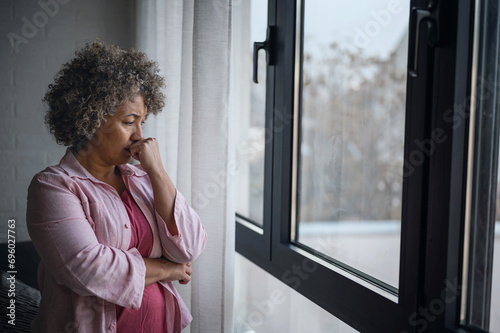 Foto A mature woman of mixed race looking outside a large window, her expression refl