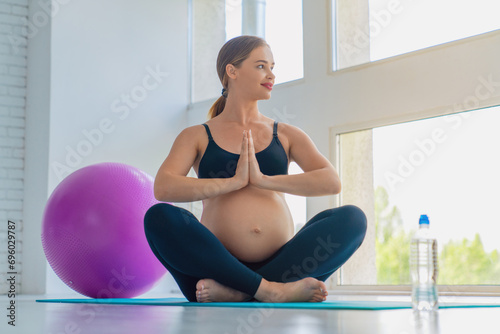 Full length portrait of young pregnant woman doing yoga and meditating during workout at home with copy space