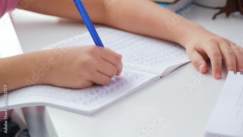 Close-up of little girl learning Chinese at home, writing hieroglyphs in the notebook. Remote education concept photo