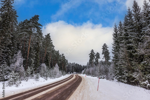 Beautiful view of winter landscape with road passing through forest against backdrop of blue sky with white clouds on frosty day. Sweden. photo