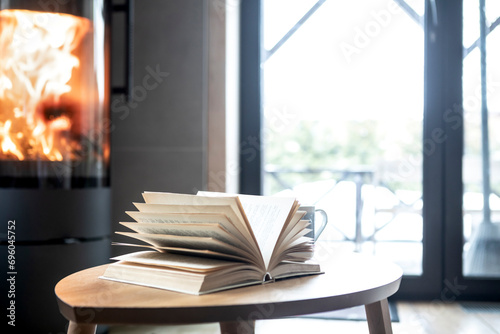 Close up photo of open book is on the coffee table near fireplace in the cozy home	 photo