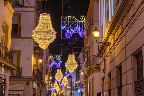 Christmas lights decoration in Sierpes street in the shape of a golden Empire style crystal candelabra, in the center city of Seville, Andalusia, Spain. Selective focus in the nearest line of lights photo