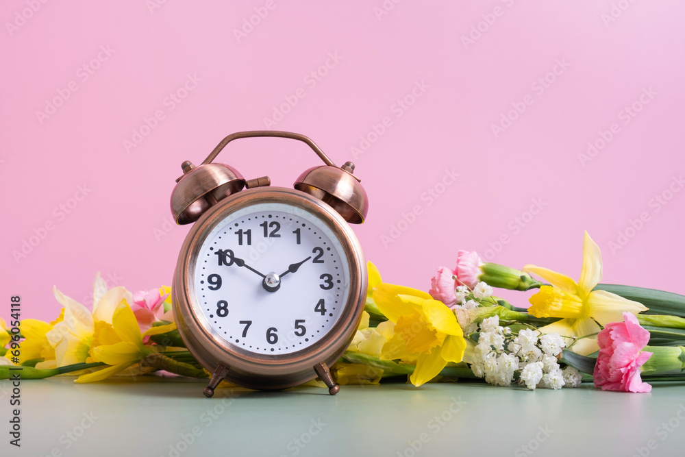 Alarm clock with spring flowers. Spring time, daylight savings concept, spring forward - obrazy, fototapety, plakaty 