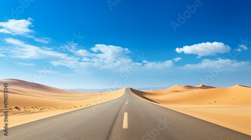 A desert highway stretching into the horizon  surrounded by golden sand dunes and a clear blue sky.