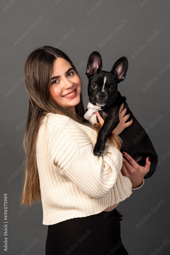 Obraz premium A beautiful young Latina woman holding a French Bulldog puppy smiling at the camera.