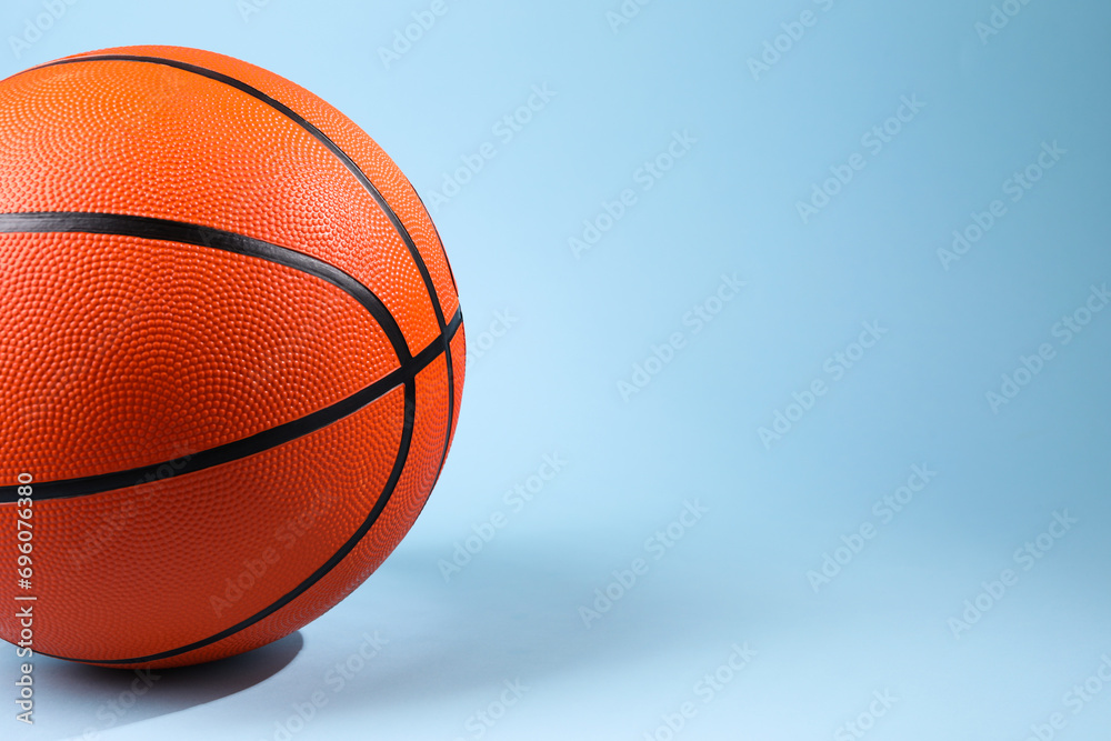 One orange basketball ball on light blue background, closeup. Space for text