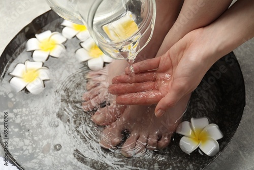 Woman pouring water onto hand while soaking her feet in bowl on floor, above view. Spa treatment photo