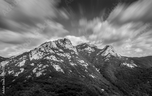 Ansel Adams inspired black and white shot of mountains in Bukhansan National Park during day. Photo was taken with long exposure, as result of that clouds a blurred and movement of them is visible. photo