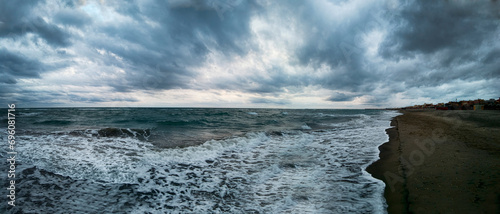 Awesome panoramic 180 degrees of rough sea at sunset on blue hour at  beach, a dramatic sky with amazing light and cloudscape and sun reflections with on water edge crashing with foam
