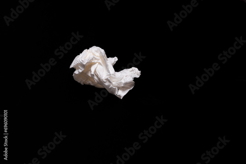 A crumpled up white facial tissue against a black backdrop