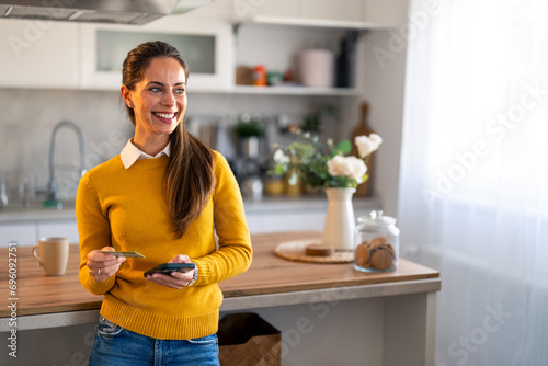 Schilderij op canvas Portrait photo of successful businesswoman looking aside with smile while holding credit card and mobile phone at home
