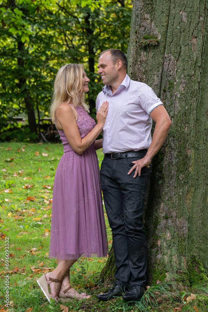 Portrait of a romantic, loving couple. A man and a woman are standing near a large tree. A woman in a beautiful pink dress. A happy family.