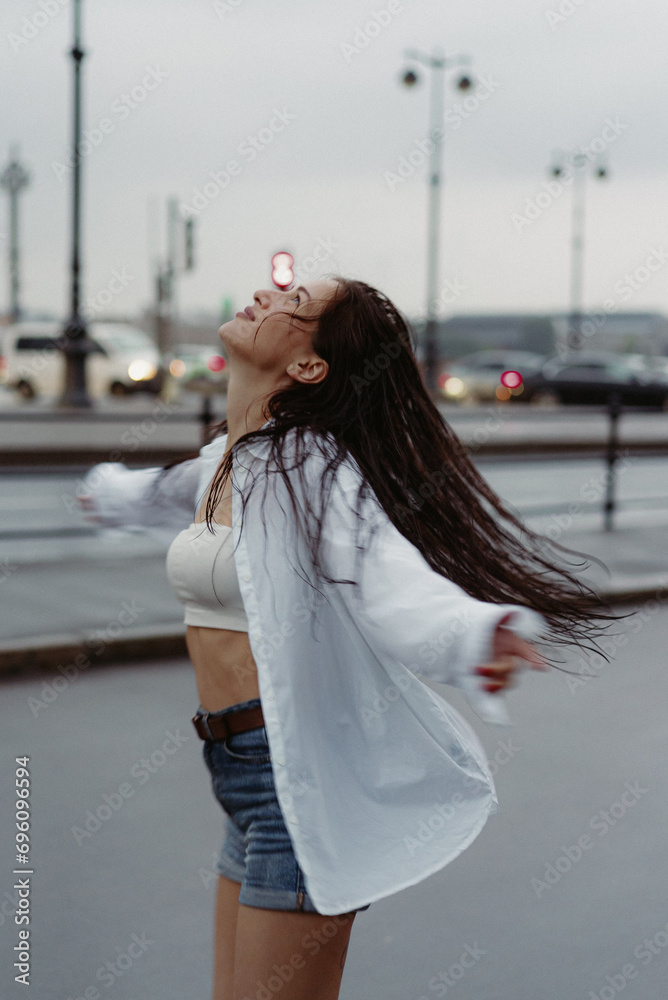 Woman walking down street in rainy weather in white shirt and blue jeans shorts Woman walking down street in rainy weather in white shirt and blue jeans shorts