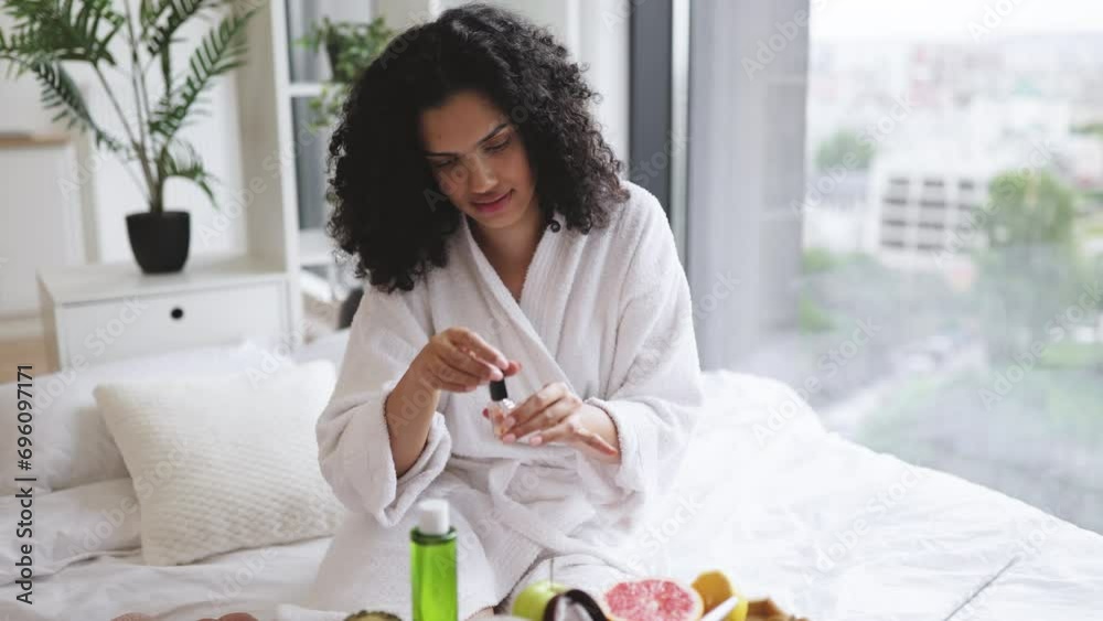 Portrait of female in white bathrobe making manicure while prepared ingredients for skin care in bright bedroom of apartment. Joyful housewife increasing life satisfaction by paints nails with polish. Portrait of female in white bathrobe making manicure while prepared ingredients for skin care in bright bedroom of apartment. Joyful housewife increasing life satisfaction by paints nails with polish.