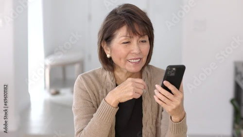 Happy attractive stylish woman holding mobile cell phone smiling laughing enjoying video chatting FaceTime sitting at home.