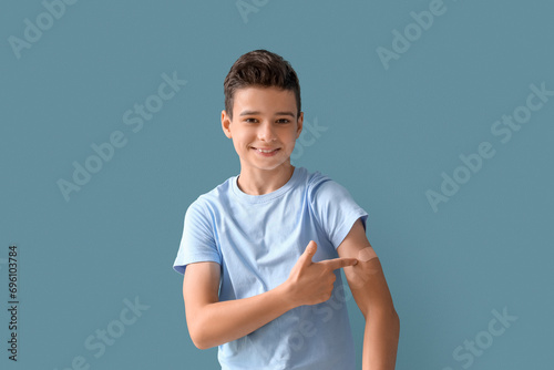 Little boy pointing at plaster after vaccination on blue background photo
