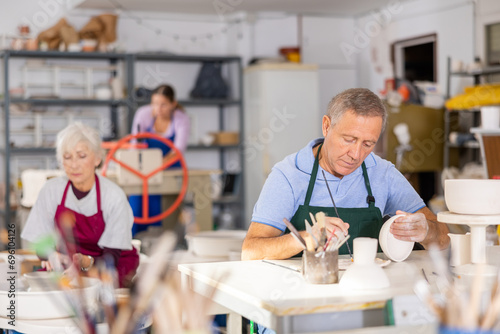 Mature craftsman painting a clay plates acrylic paints in art studio